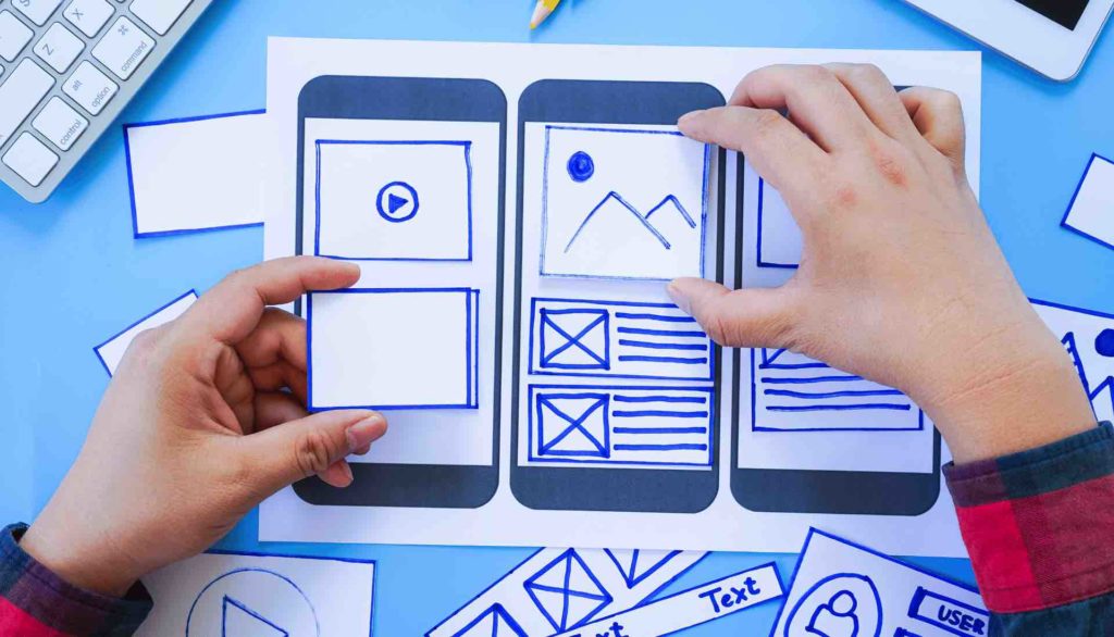 Person designing mobile responsiveness on a board using various cut-out shapes.